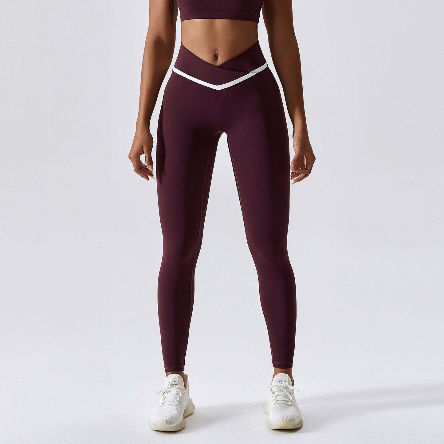 Woman wearing maroon leggings with a white waistband on a light gray background